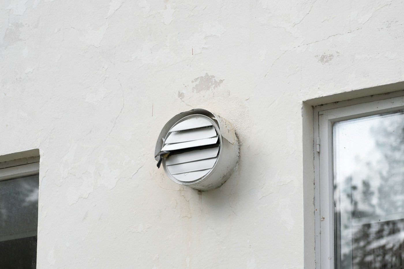 Bouche de ventilation ronde sur un mur blanc, près d'une fenêtre