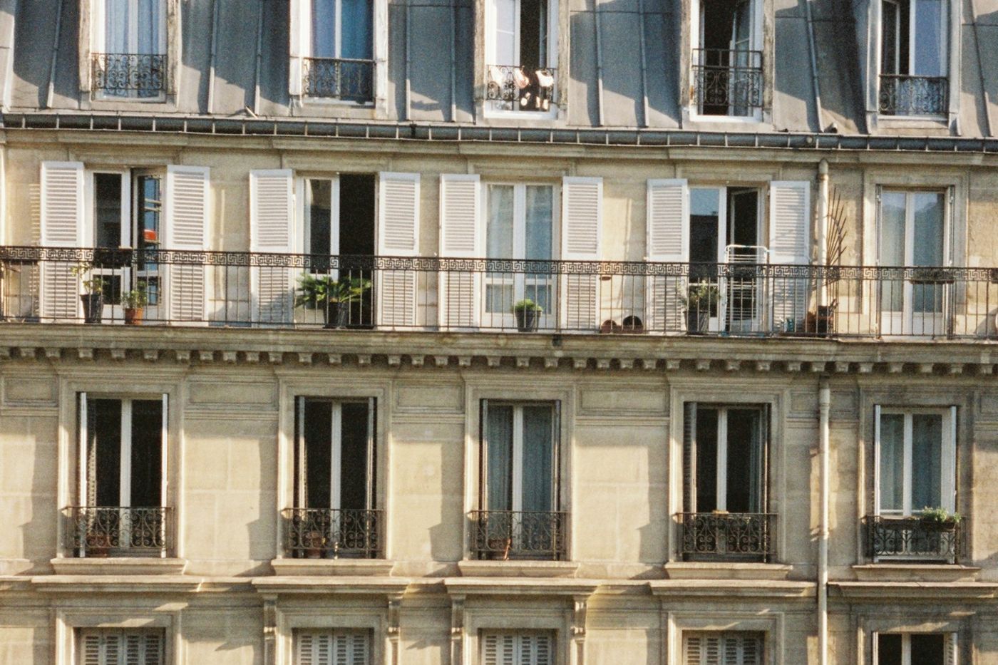 Façade d'immeuble ancien en pierre de taille, balcons en fer forgé, persiennes et fenêtres ouvertes au soleil